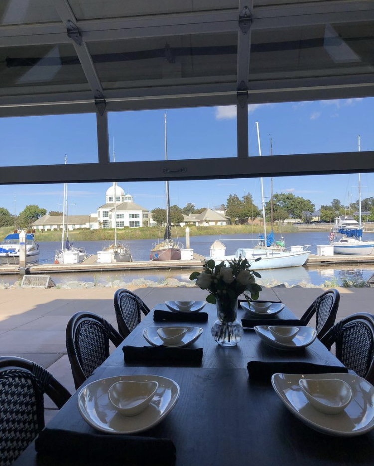 The outdoor padio table setup with flowers on tables and showcases the waterfront in the backdrop.